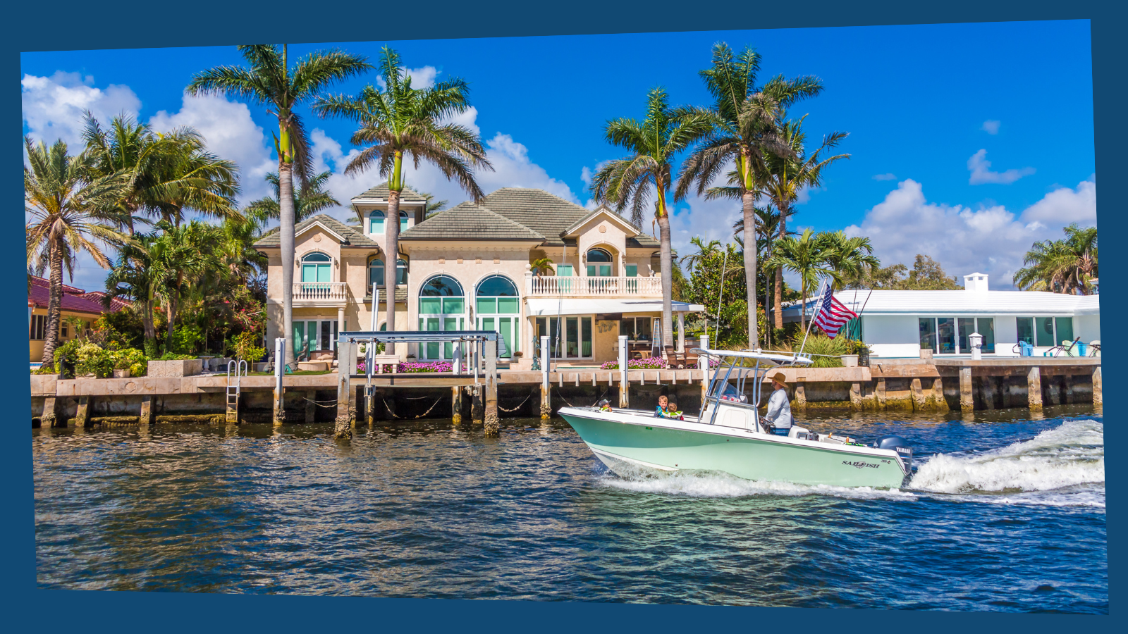 A mansion on the water surrounded by palm trees. A motor boat is in the foreground.